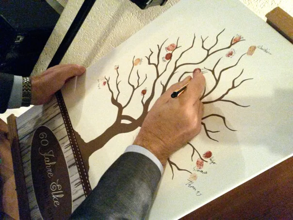 Gästebaum zum 60. Geburtstag: Gast schreibt seinen Namen neben einen Fingerabdruck