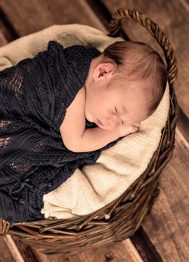 Neugeborenes im Weidenkorb | Peter Lauritis Photography Neugeborenes im Weidenkorb: schlafendes Baby in dunkelblauem Stricktuch auf heller Decke