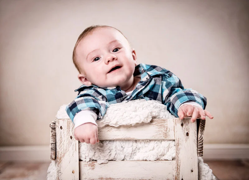 Baby in der Holzkiste | Peter Lauritis Photography Babyfotos mit guter Laune: strahlendes Baby im karierten Hemd in einer weißen Holzkiste