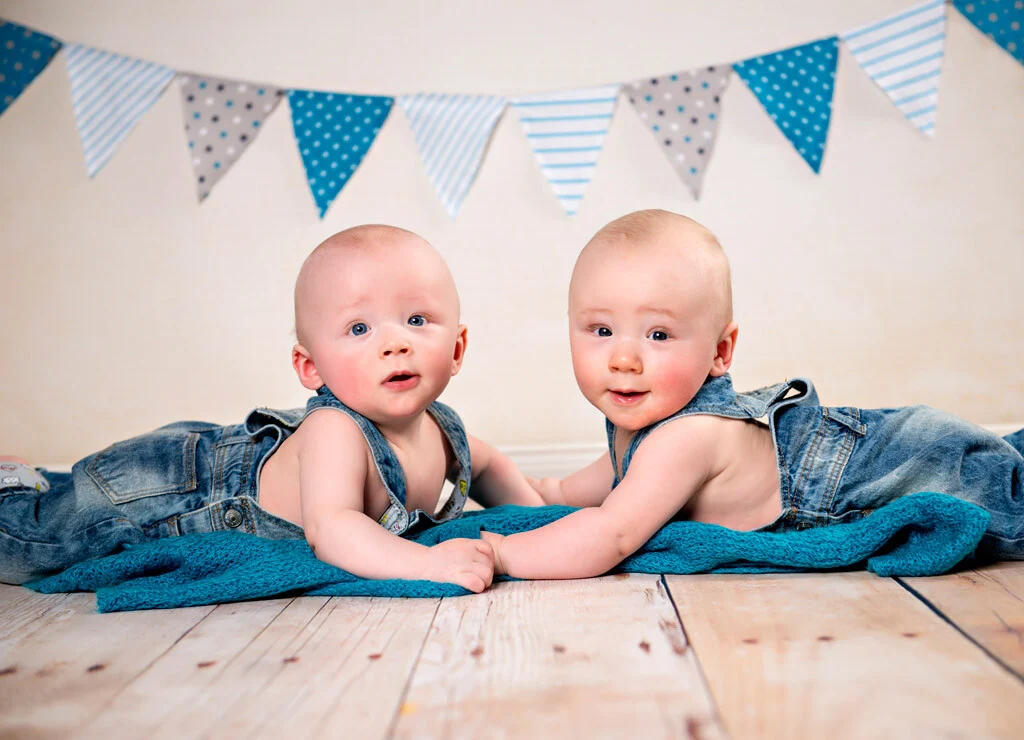 Babyzwillinge | Peter Lauritis Photography Babyzwillinge im Fotostudio: zwei Babys in Jeanslatzhosen unter einer Wimpelkette
