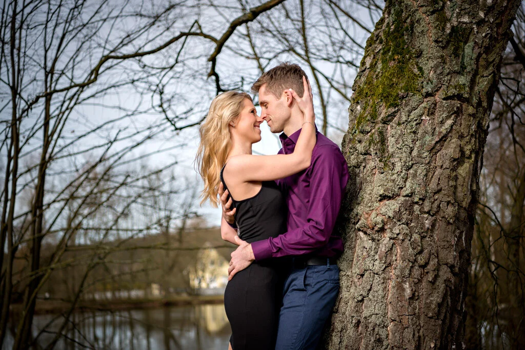Paar am Baum | Peter Lauritis Photography Engagement-Fotoshooting: Paar lehnt lächelnd an einem dicken Baumstamm am Wasser