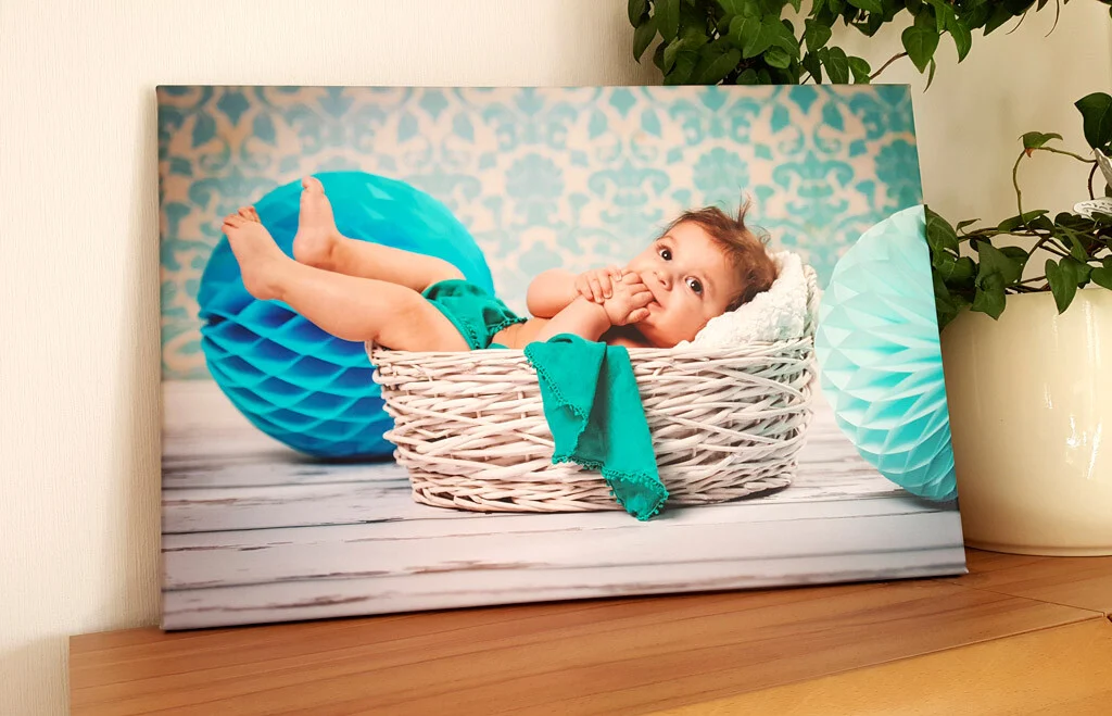 Babyfoto auf Leinwand | Peter Lauritis Photography Babyfoto auf Leinwand: Baby im Weidenkorb vor türkisfarbenen Wabenbällen auf einem Sideboard