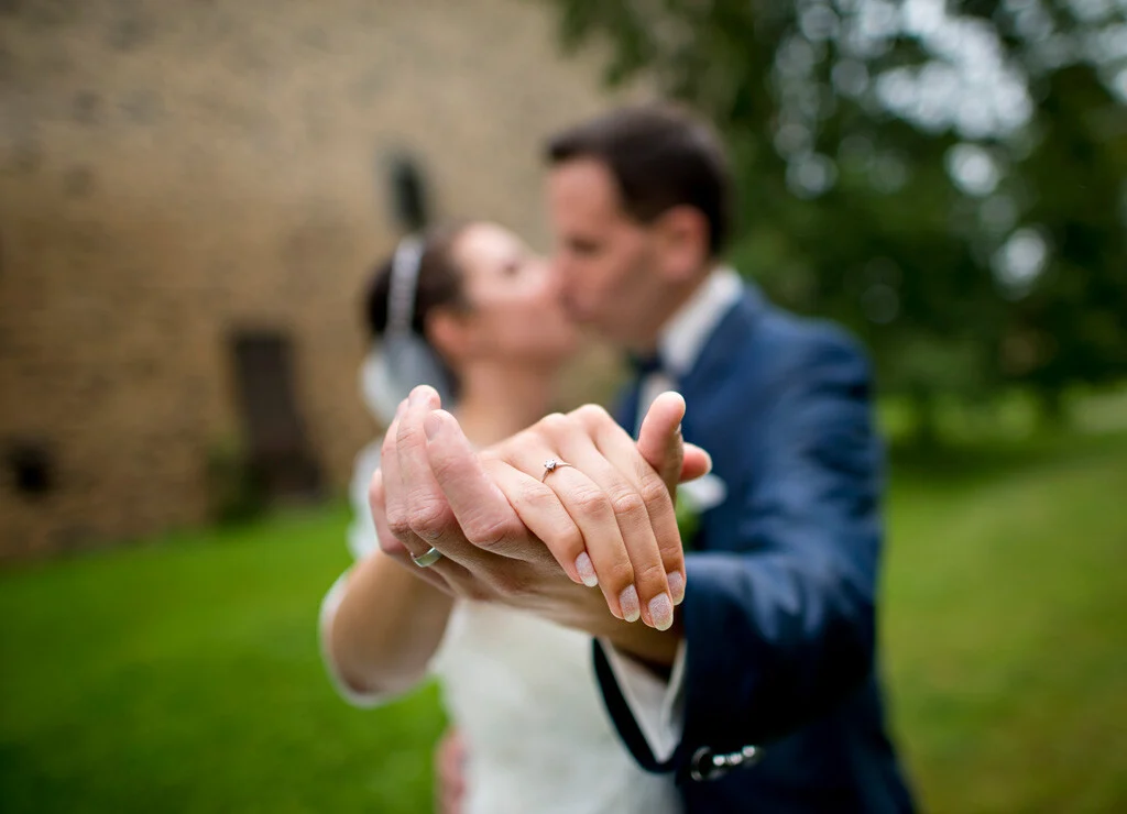 Ringe im Fokus | Peter Lauritis Photography Hochzeit im Schloss Romrod: Hände mit Eheringen im Fokus, dahinter küsst sich das Brautpaar