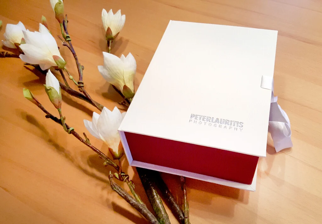 Hochzeitsbox: weiße Box mit rotem Innenteil und Logo neben Zweigen mit Magnolienblüten
