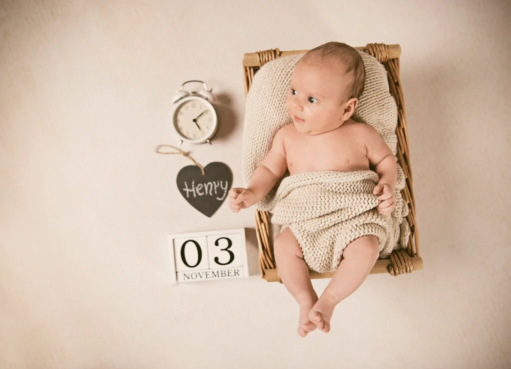 Baby im Weidenkörbchen | Peter Lauritis Photography Neugeborenenfotos mit Datum: Baby im Weidenkörbchen neben Wecker, Namensherz und Datumswürfeln