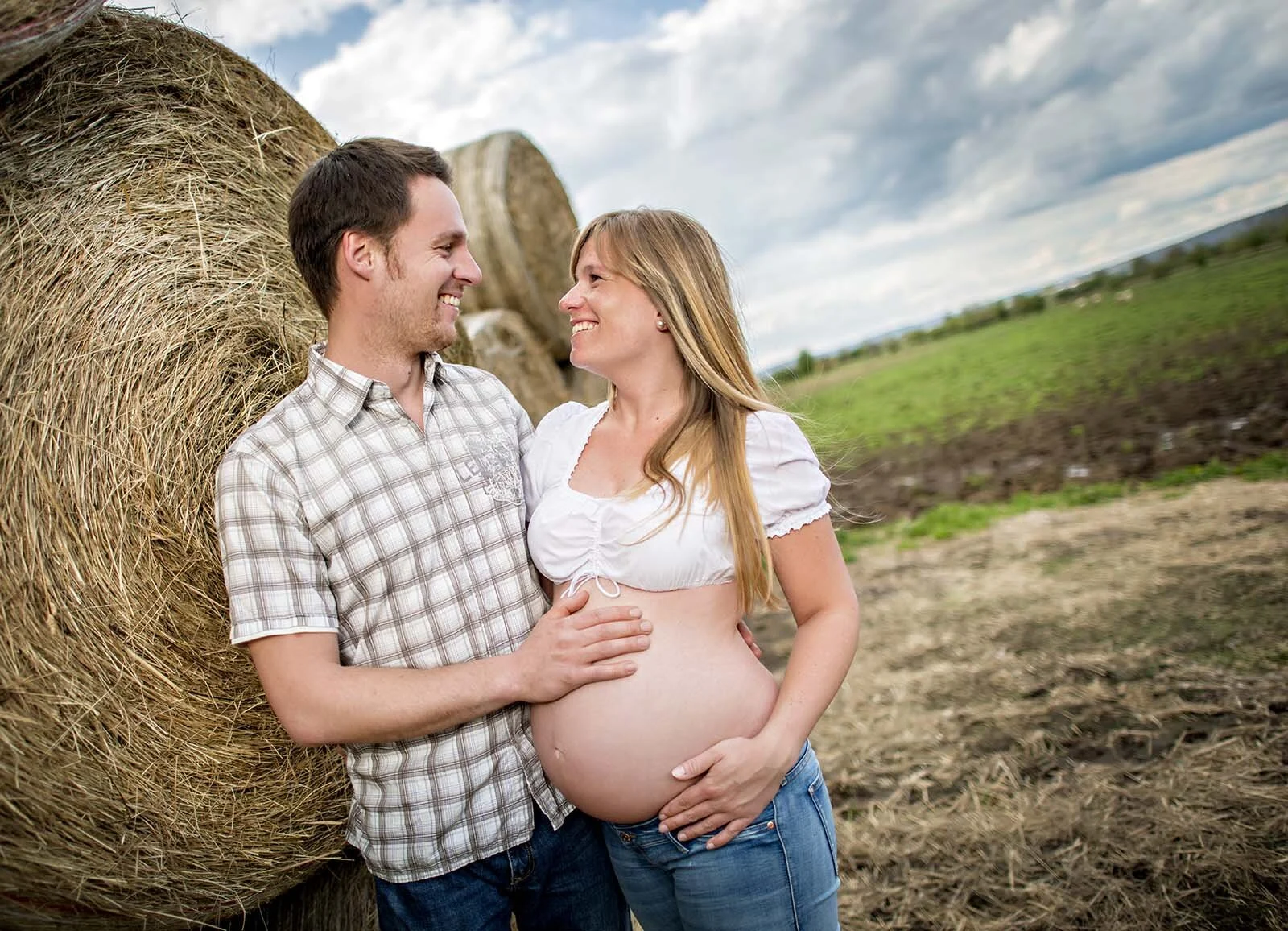 Am Strohballen | Peter Lauritis Photography Babybauchfotos am Strohballen: werdende Eltern lehnen lachend an einem großen Strohballen