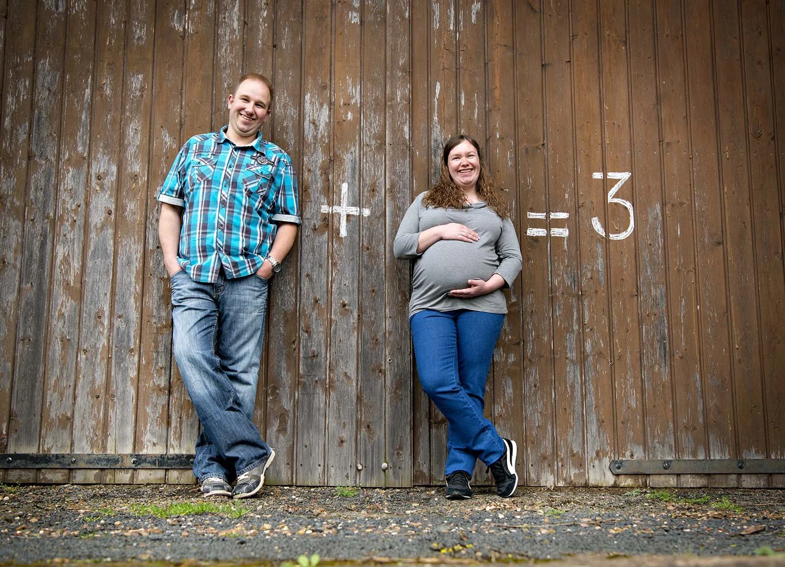 1 + 1 = 3 | Peter Lauritis Photography Lustiges Babybauchshooting: Paar vor Holzwand mit Kreidezeichen Plus und gleich drei