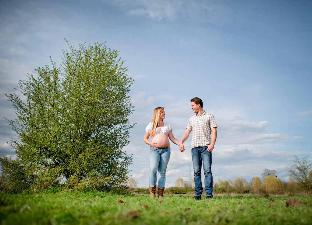 Hand in Hand | Peter Lauritis Photography Frühlings-Outdoorshooting: werdende Eltern gehen Hand in Hand über eine Wiese neben einem Baum