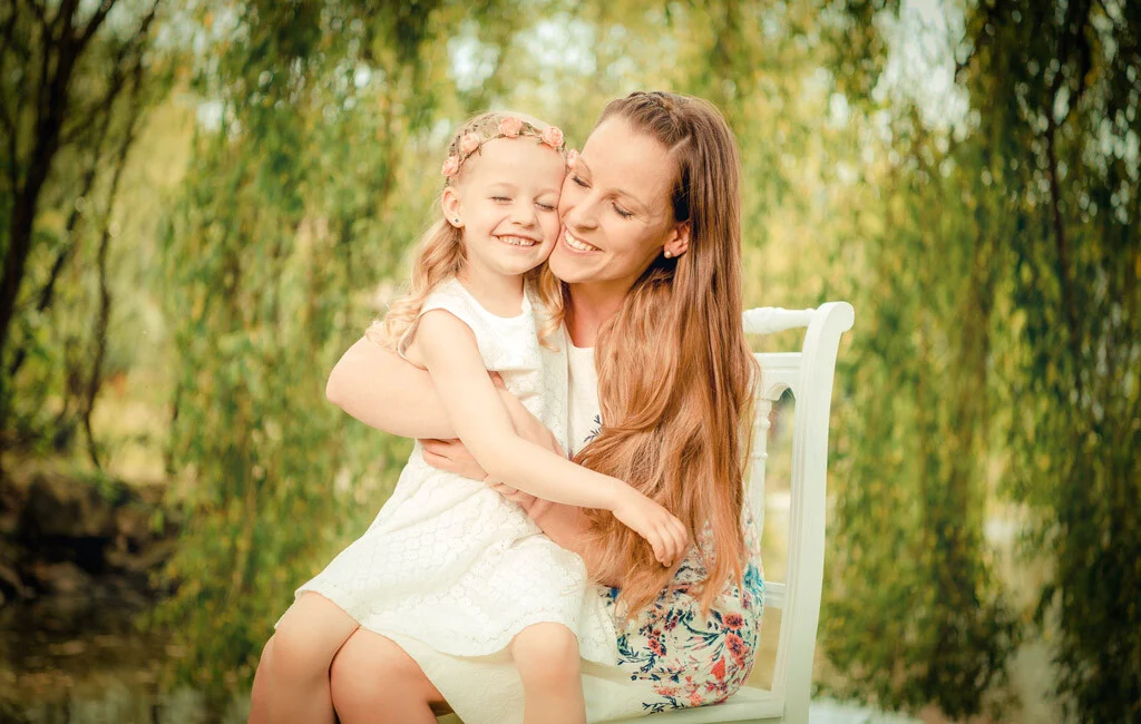 Mama und Tochter | Peter Lauritis Photography Mama-Tochter-Fotos: Tochter kuschelt sich lächelnd an ihre Mutter auf einer weißen Bank im Grünen