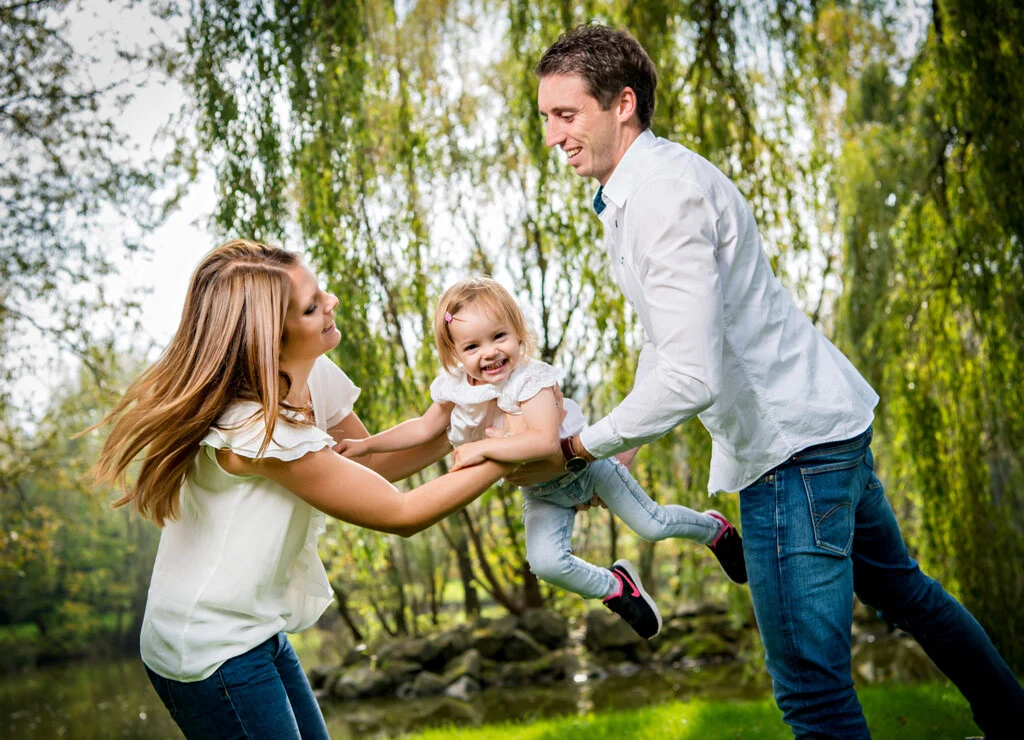 Durch die Luft | Peter Lauritis Photography Familienfotos mit Action: Eltern schwingen ihre lachende Tochter vor einer Trauerweide