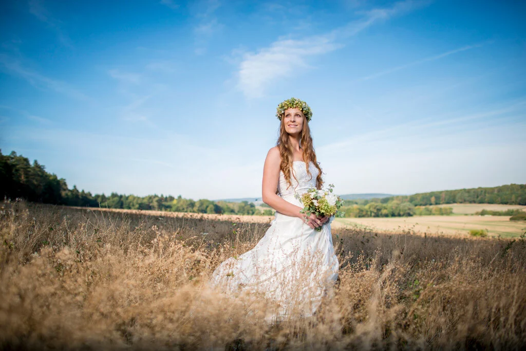 Fotoshooting im Brautkleid: Frau mit Blumenkranz und Strauß steht auf einem goldenen Feld