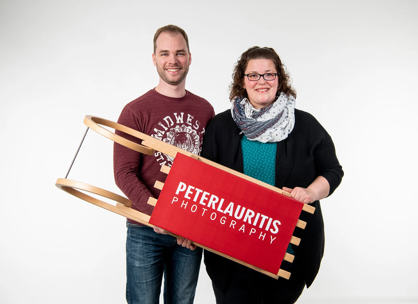 Schlitten-Übergabe | Peter Lauritis Photography Advents-Gewinnspiel: Mann und Frau halten einen Holzschlitten mit rotem Peter-Lauritis-Logo