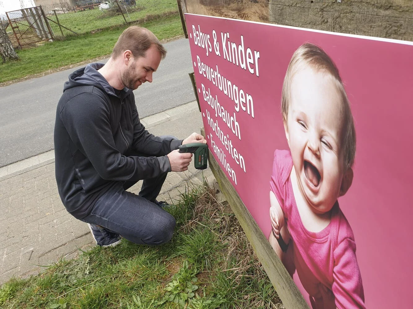 Mann befestigt das Werbebanner an einem Zaun direkt an der Straße