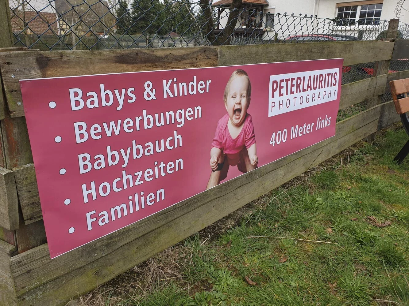Pinkes Werbebanner mit lachendem Baby und Leistungen an einem Holzzaun