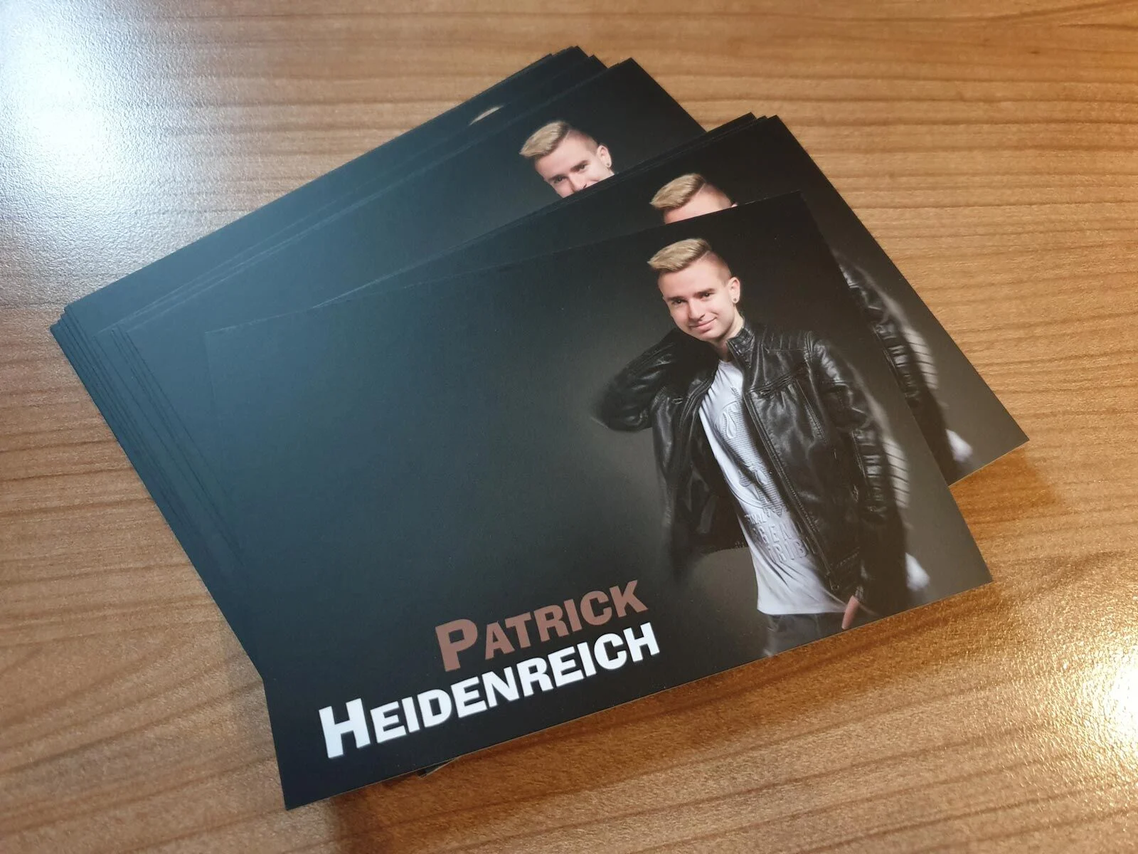 Neue Autogrammkarten von Patrick Heidenreich mit Portrait in Lederjacke auf einem Holztisch