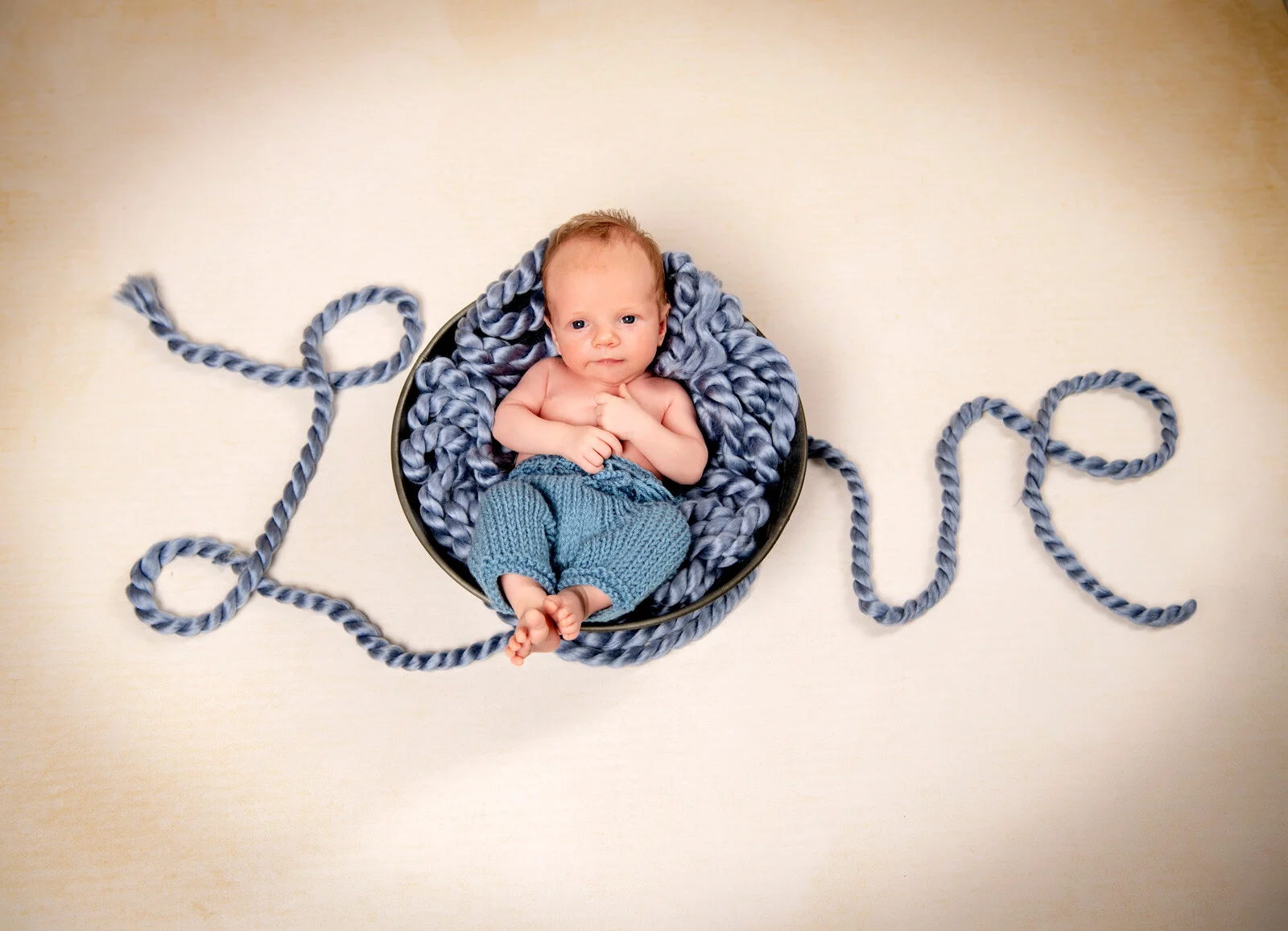 Love | Peter Lauritis Photography Neugeborene im Fotostudio: Baby in einer Strickschale, daneben ein Seil als Schriftzug Love