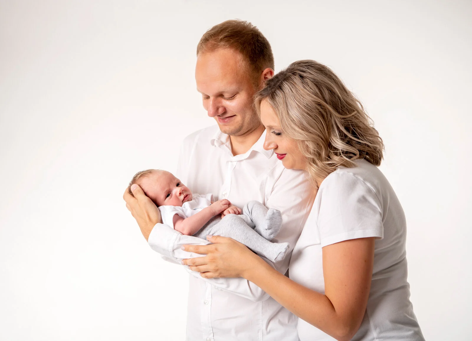 Familie zu dritt | Peter Lauritis Photography Familienfoto zu dritt: Eltern in Weiß halten ihr Neugeborenes vor weißem Hintergrund