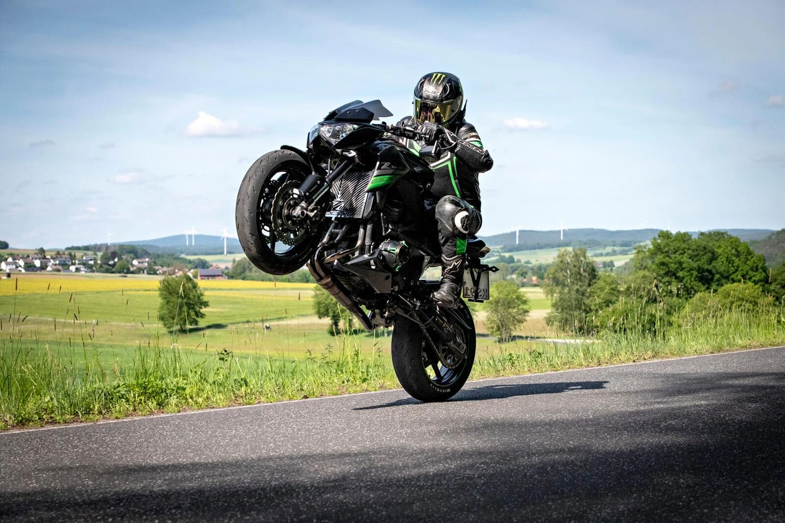 Motorradfahrer macht einen Wheelie auf einer Landstraße vor weiter Landschaft