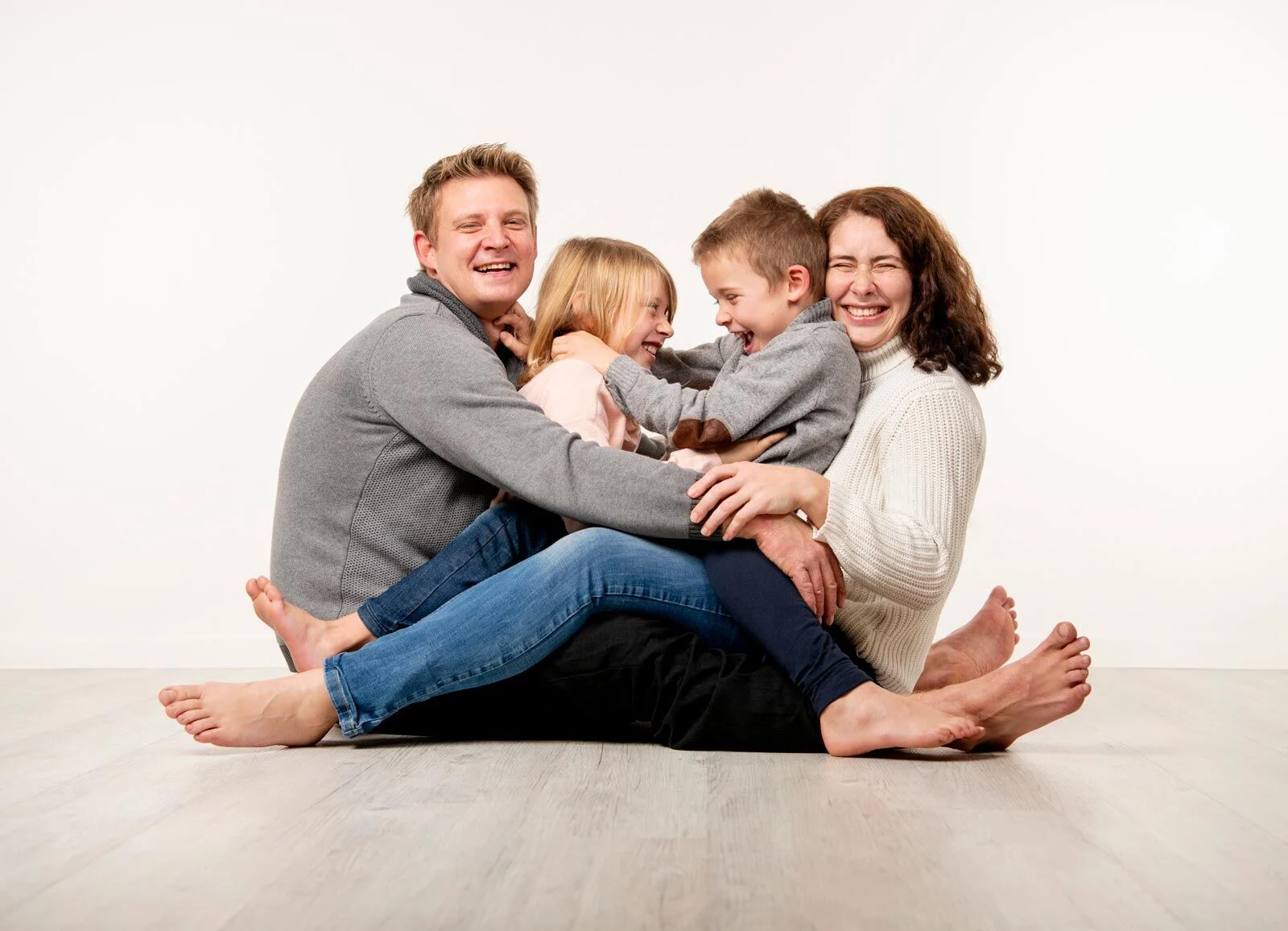 Adventszeit im Fotostudio: Eltern und zwei Kinder kuscheln lachend auf dem hellen Boden