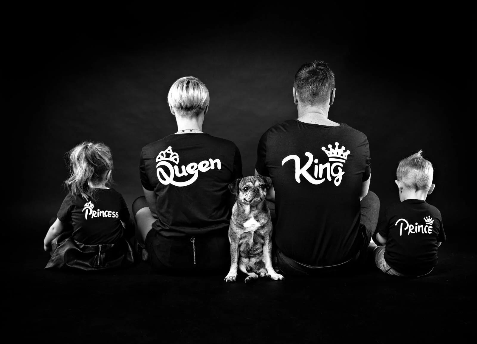 Familie von hinten in Shirts mit King, Queen, Prince und Princess, dazwischen ein Hund