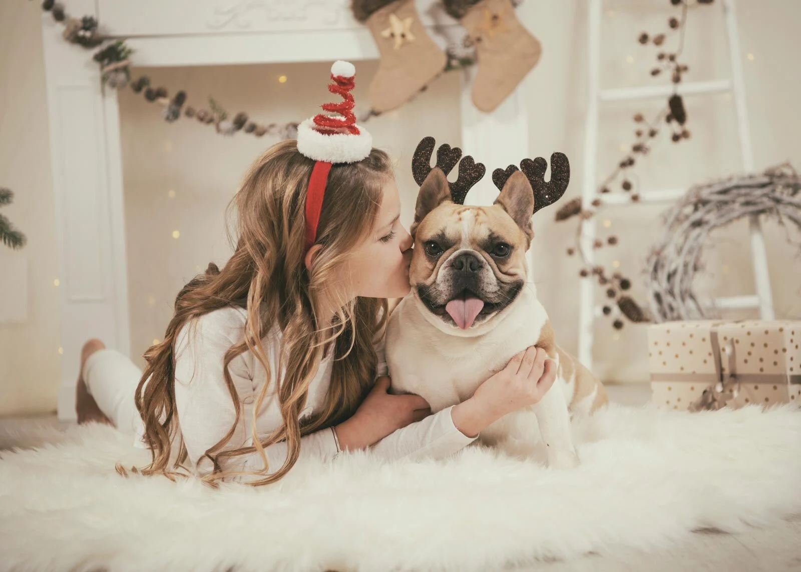 Mädchen gibt der Bulldogge mit Rentiergeweih einen Kuss auf die Wange