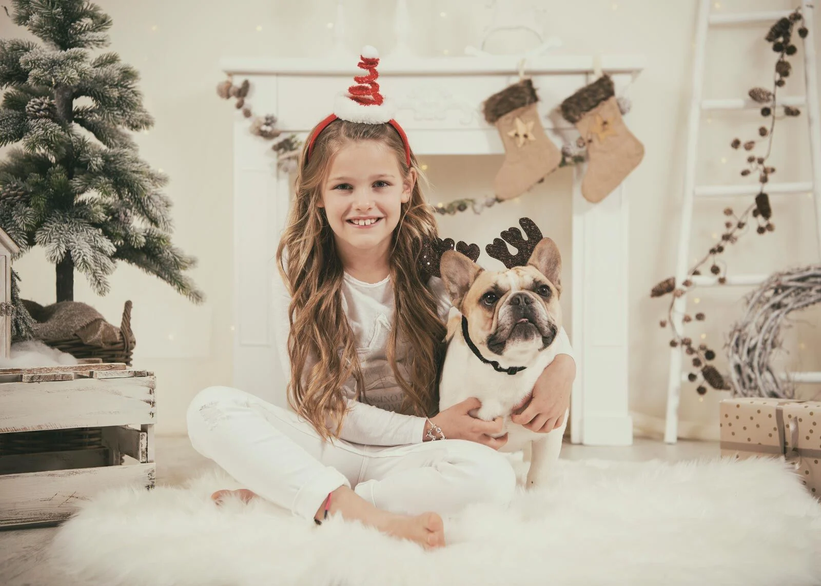 Tierfreundliches Fotostudio: Mädchen sitzt mit Bulldogge vor weihnachtlichem Kamin