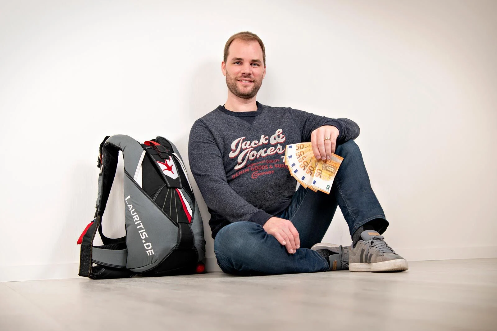 Peter mit dem Spendengeld | Peter Lauritis Photography Spende: Peter Lauritis sitzt mit Geldscheinen in der Hand neben einem Fallschirm-Rucksack