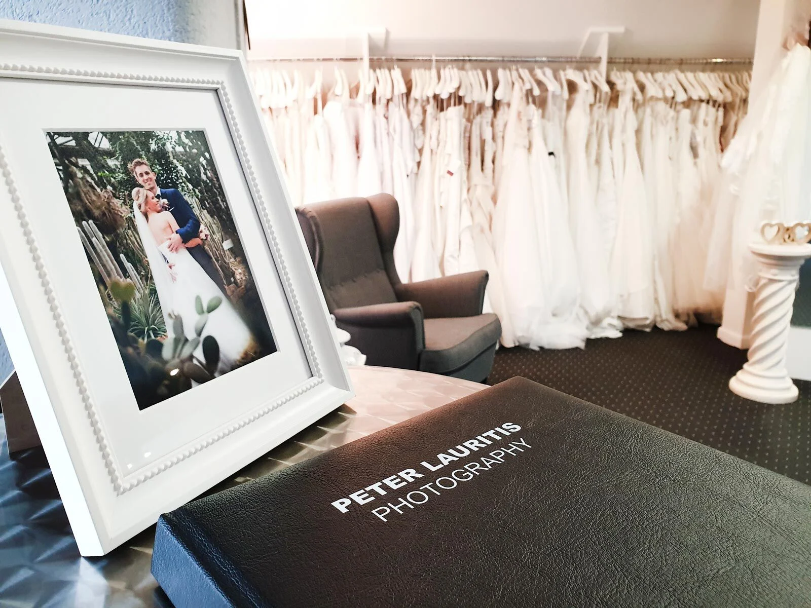 Brautmoden-Hausmesse: gerahmtes Hochzeitsfoto und Fotoalbum vor einer Reihe weißer Brautkleider