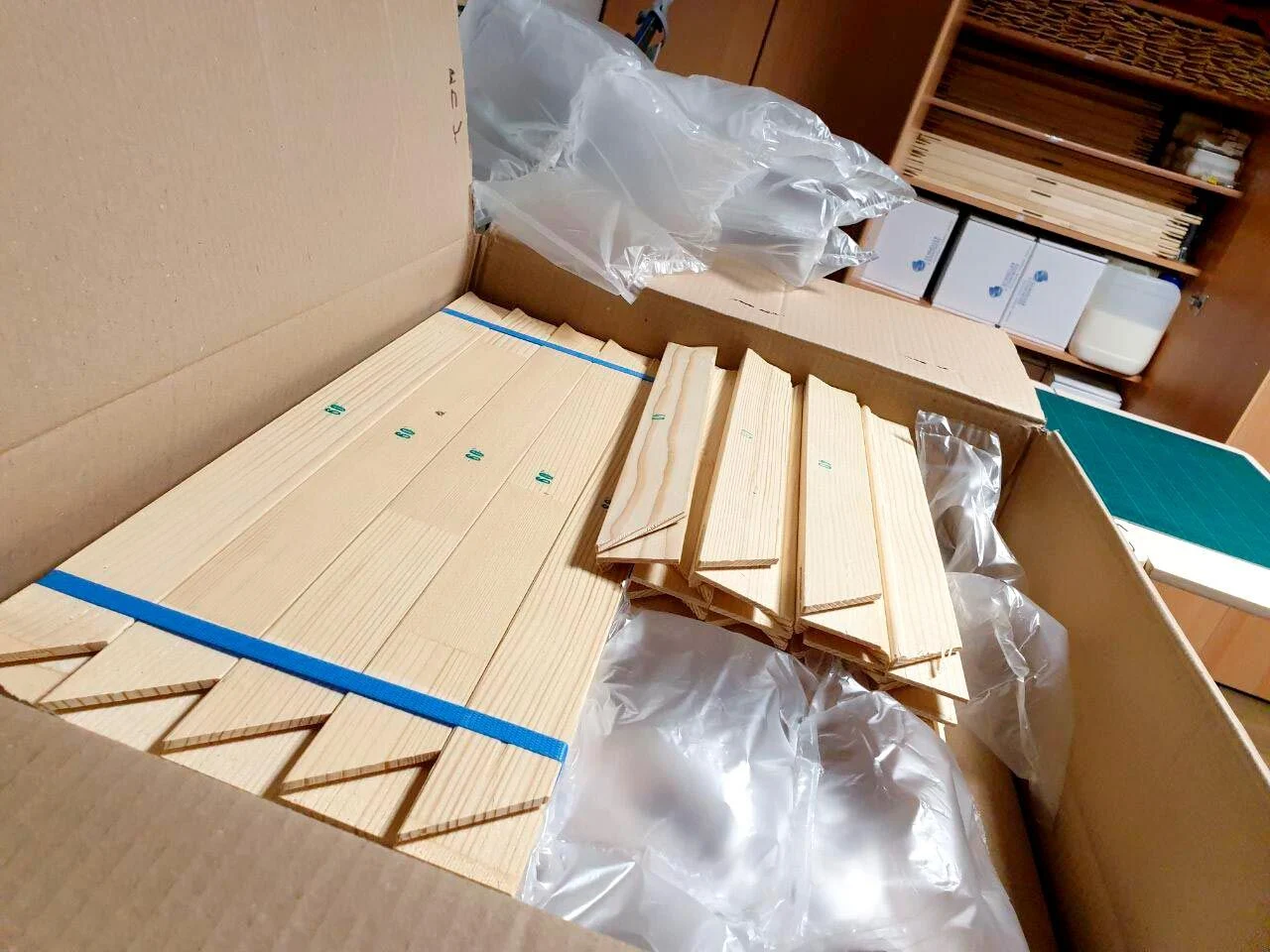 Keilrahmen-Leisten aus hellem Holz liegen verpackt in einem großen Karton
