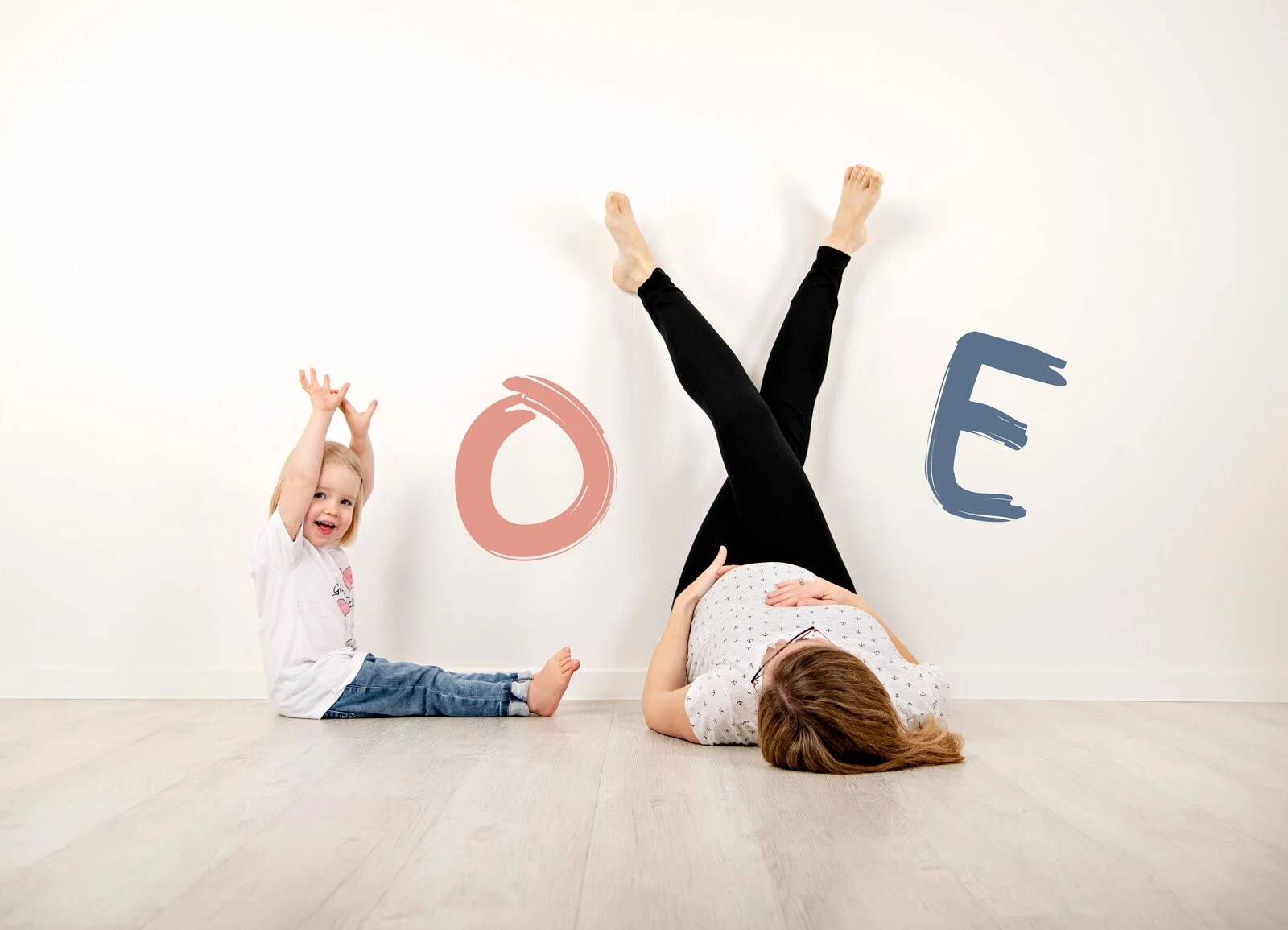 Beine hoch | Peter Lauritis Photography Babybauchfotos mit Geschwisterkind: Mama liegt mit Beinen an der Wand, die Tochter jubelt daneben