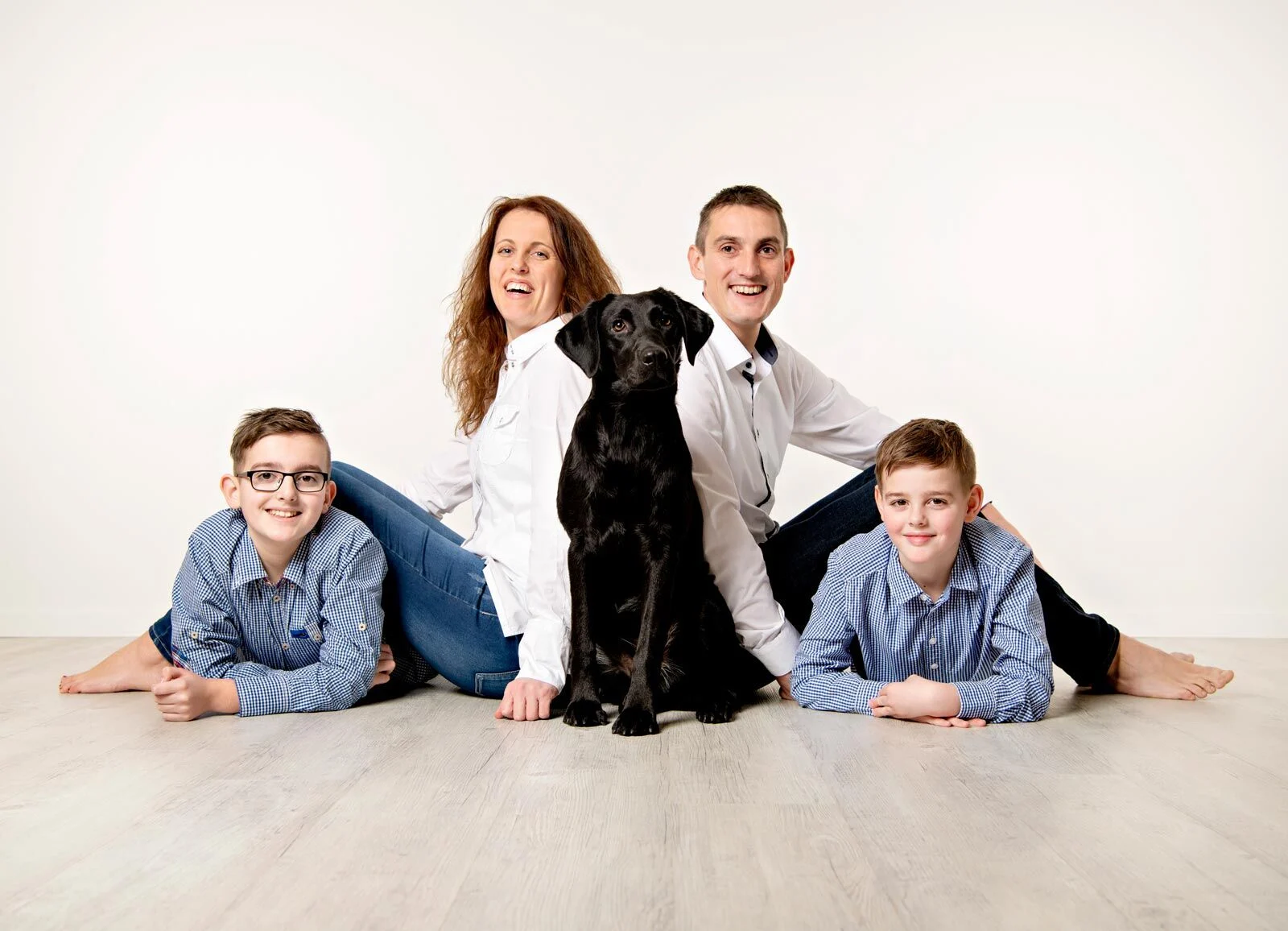 Familienshooting mit Hund: Eltern und zwei Söhne liegen mit schwarzem Hund auf dem Studioboden
