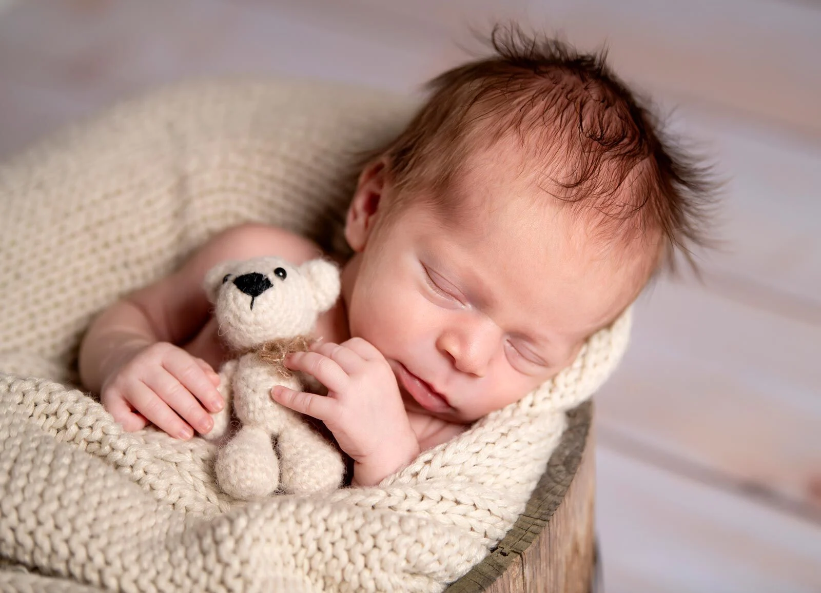 Neugeborenes schläft eingekuschelt in einer Strickdecke und hält einen kleinen Teddy