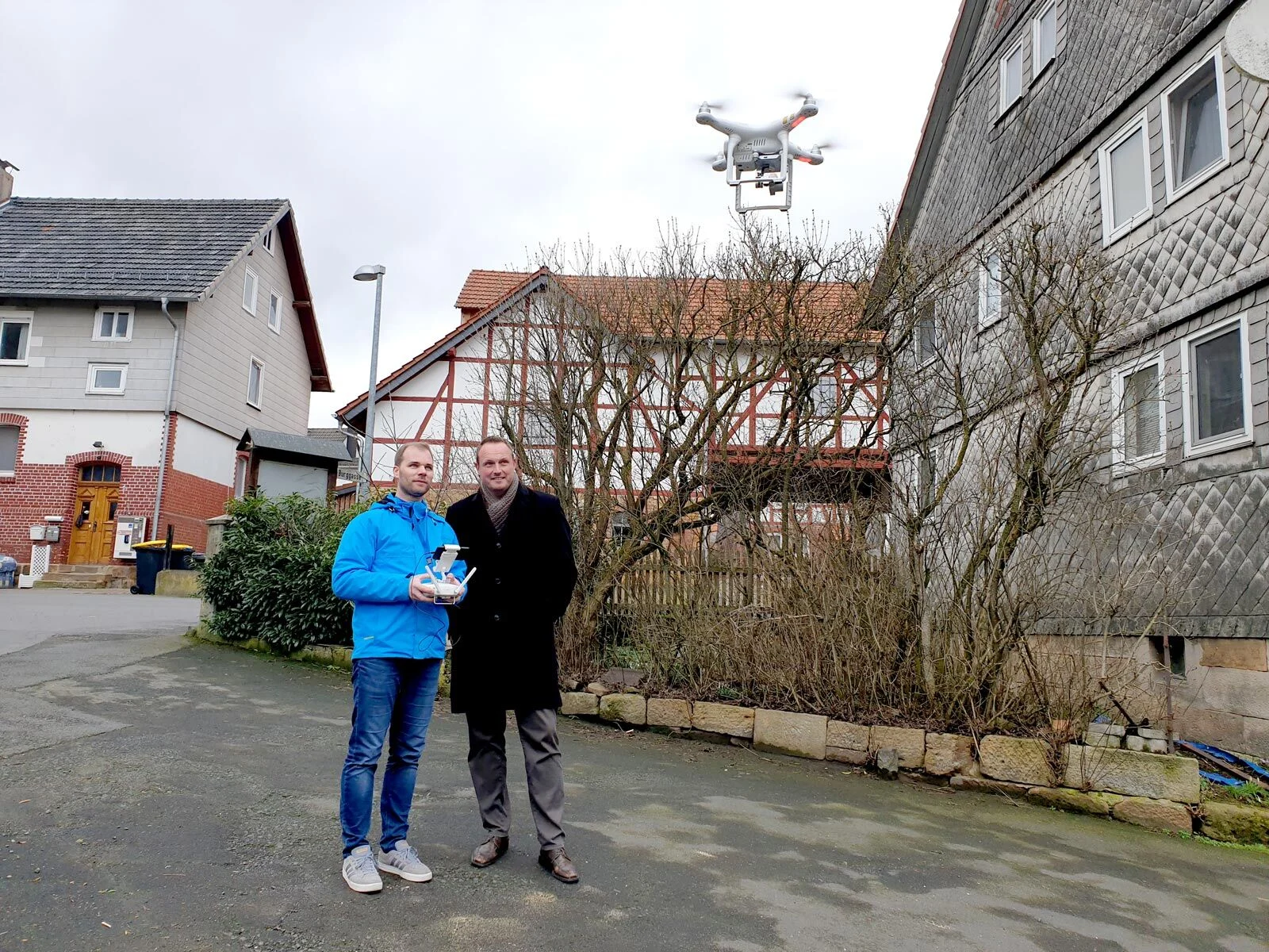 Immobilienfotos mit Drohne: Pilot mit Fernsteuerung, Drohne über einem Fachwerkhaus