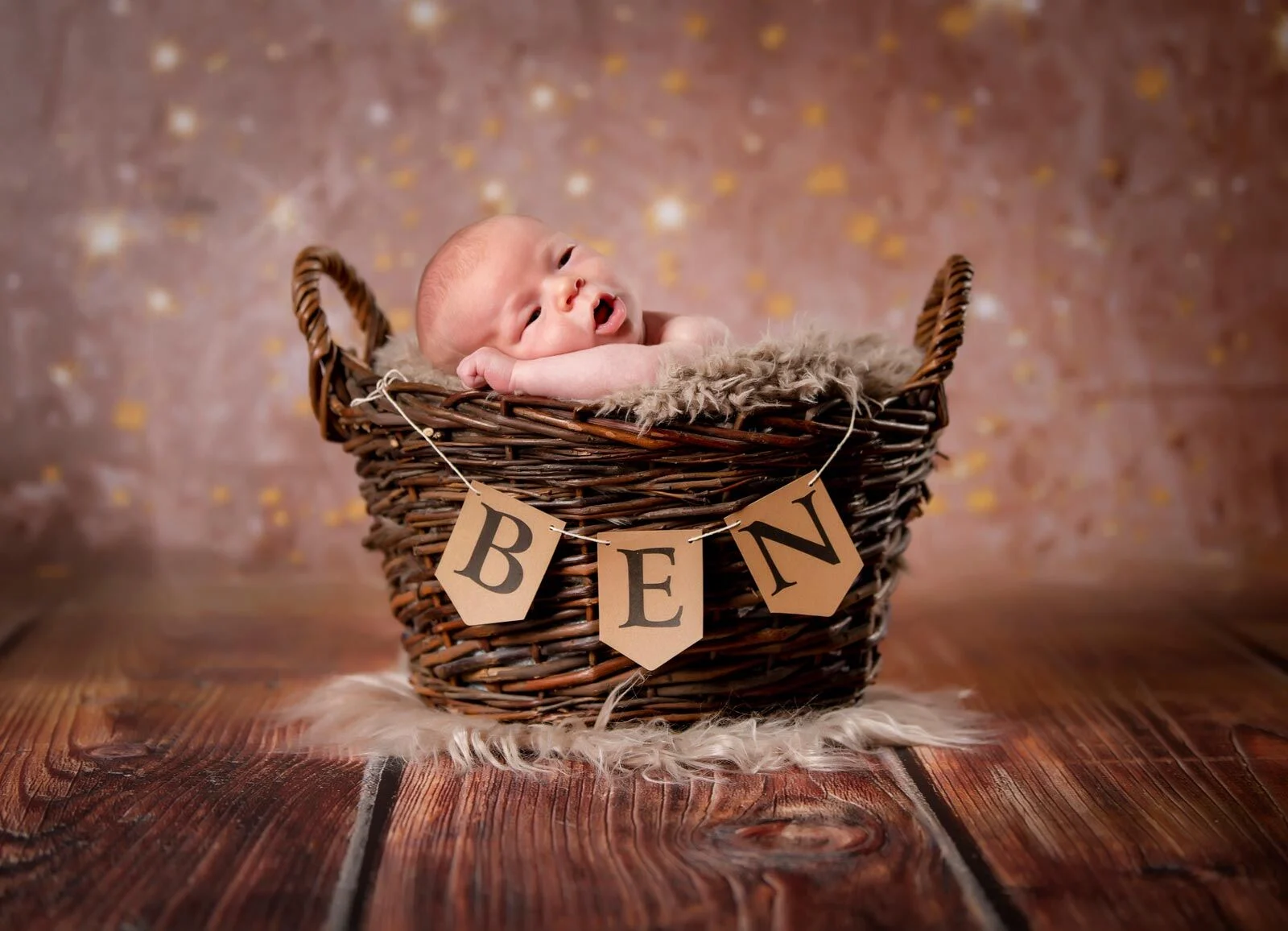 Newborn-Fotoshooting: Neugeborenes schläft in einem Weidenkorb mit Fell und Wimpelkette