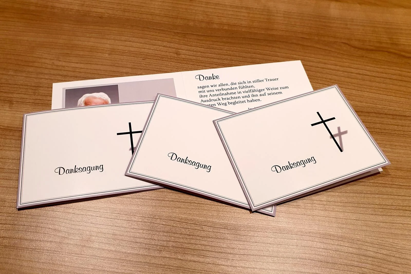Drei Dankeskarten mit der Aufschrift Danksagung und Kreuz liegen auf einem Holztisch