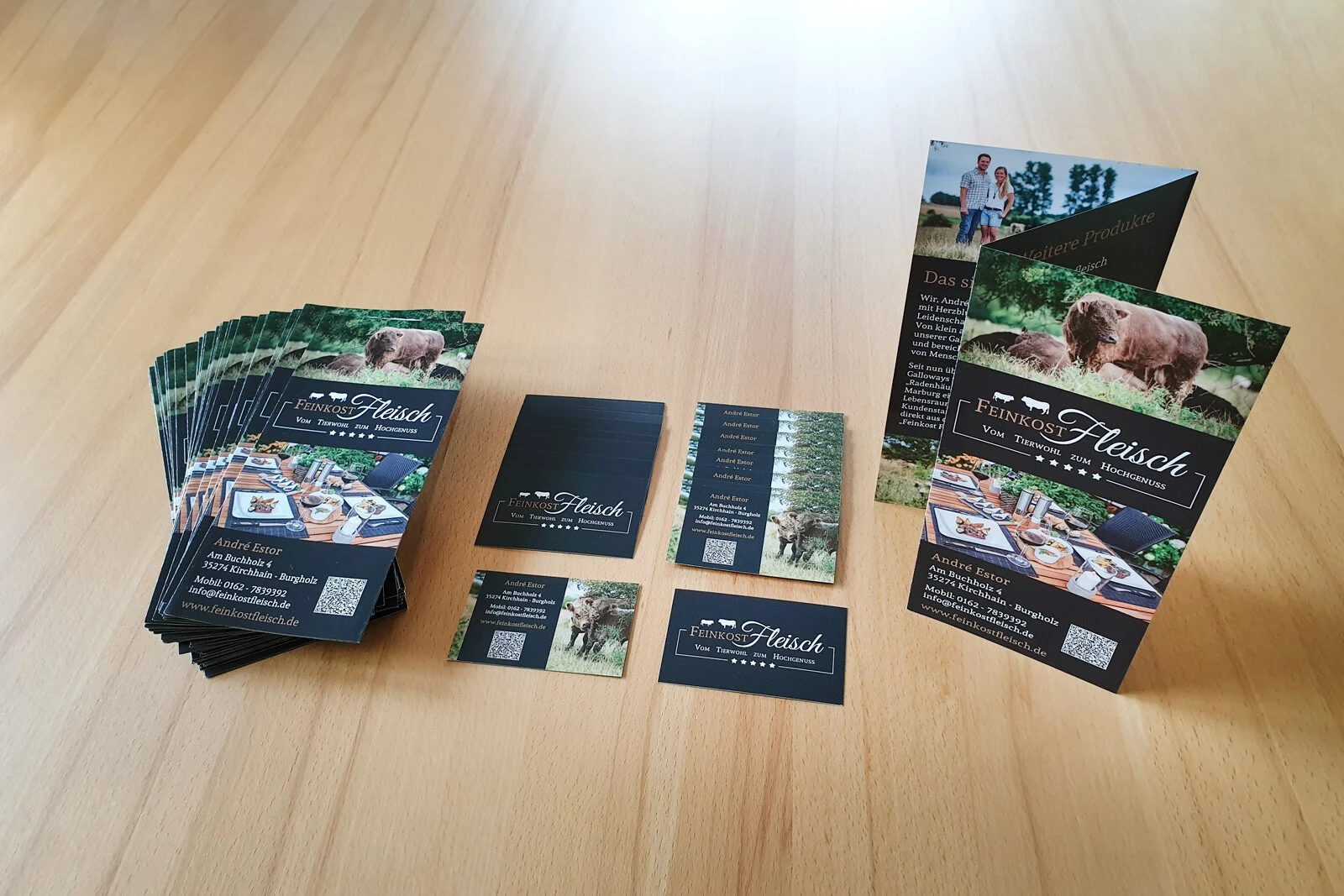 Flyer und Visitenkarten von Feinkost Fleisch liegen auf einem hellen Holztisch