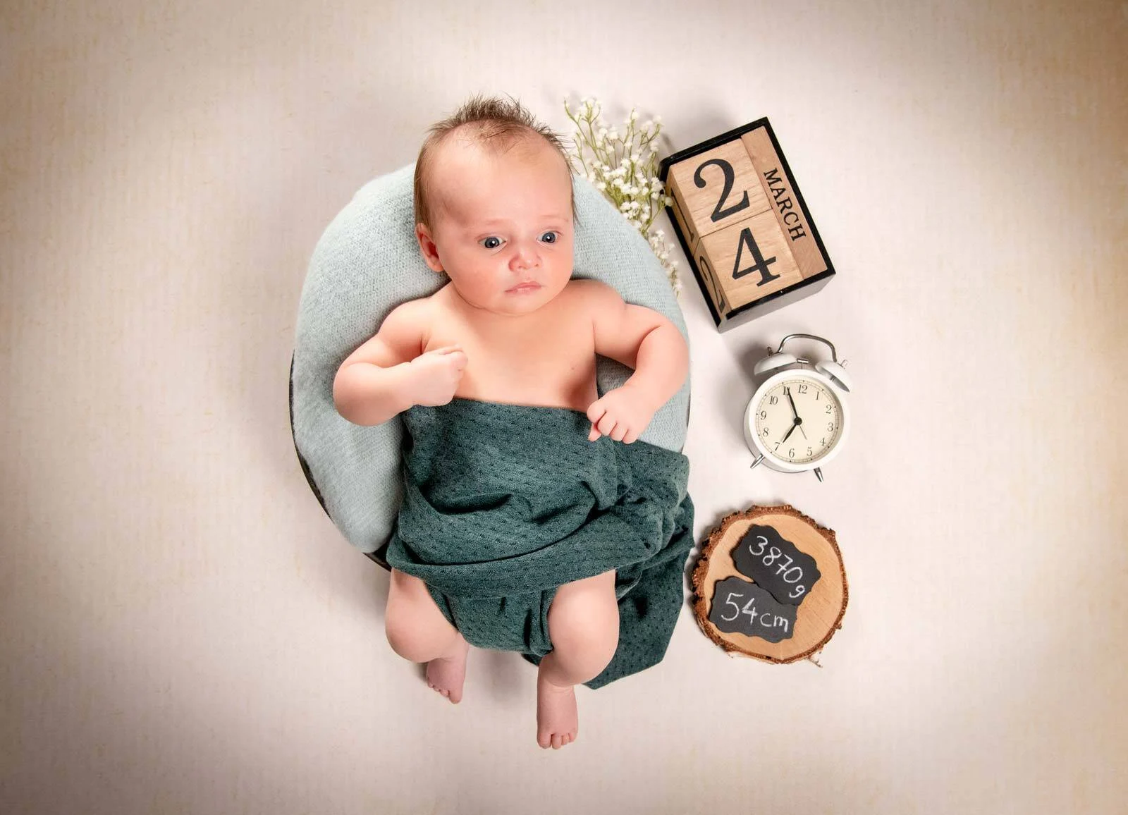 Baby im runden Körbchen von oben, daneben Datumswürfel, Wecker und eine Holzscheibe