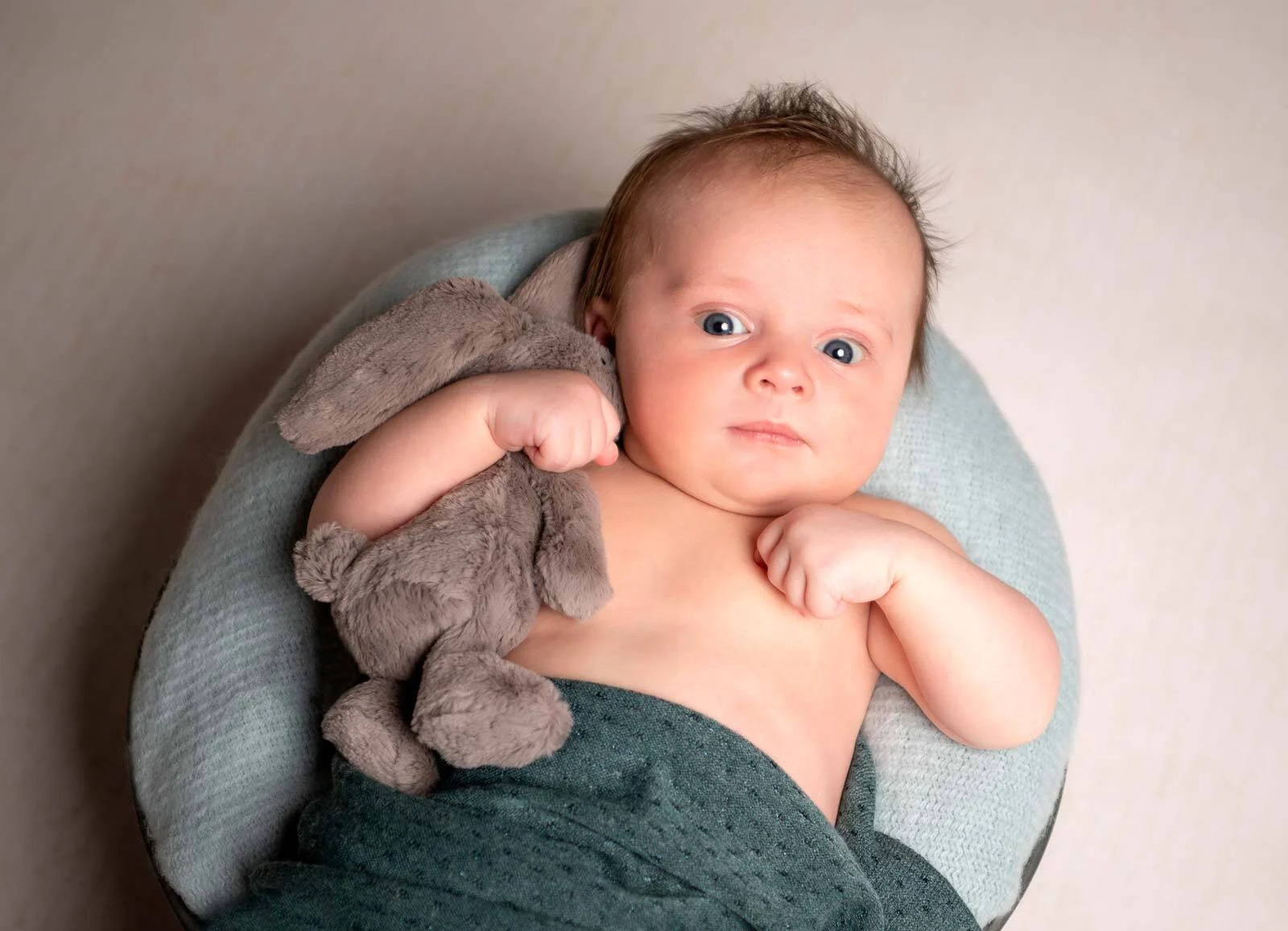 Baby mit großen Augen hält einen grauen Kuschelhasen im Arm