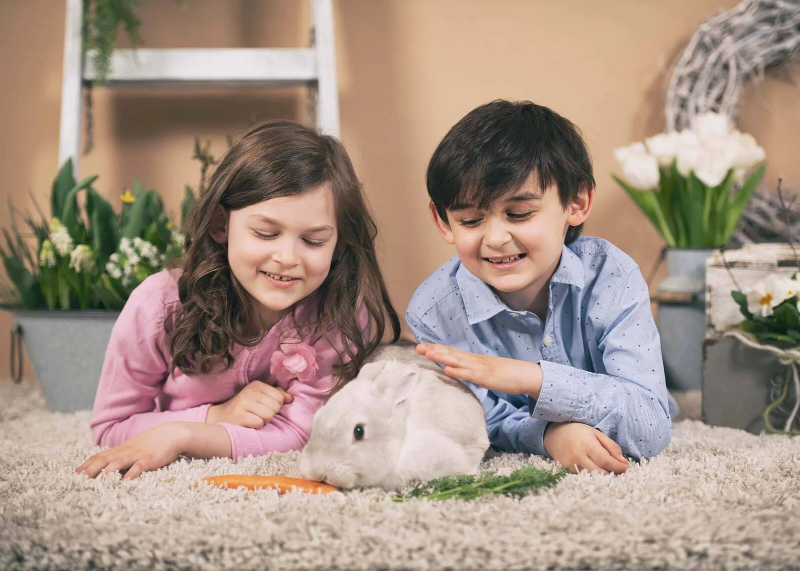 Kinderfotoaktion: Schwester und Bruder liegen auf dem Teppich und streicheln ein Kaninchen