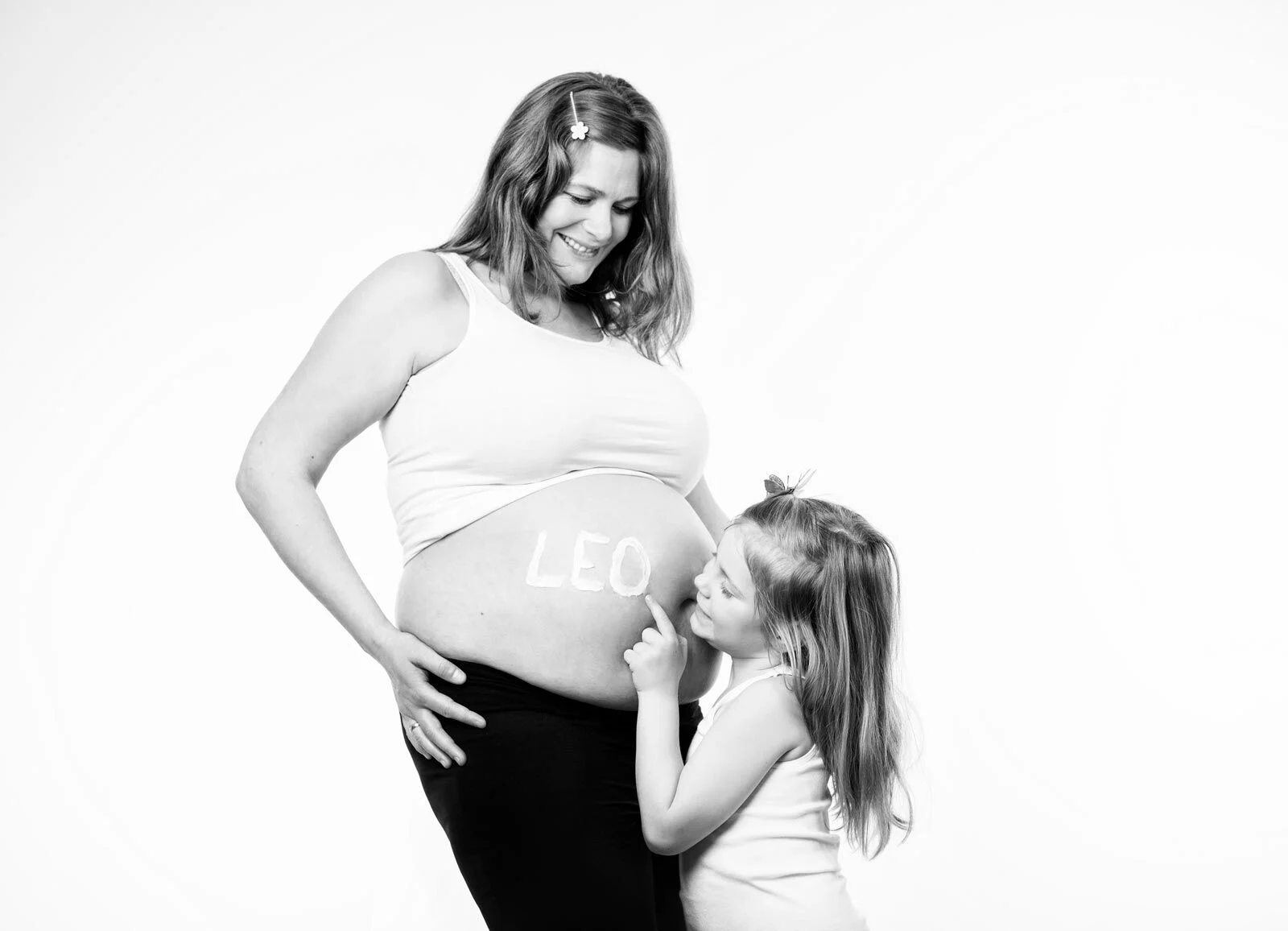Schwarz-Weiß-Foto: Mädchen gibt dem Babybauch der lächelnden Mutter einen Kuss