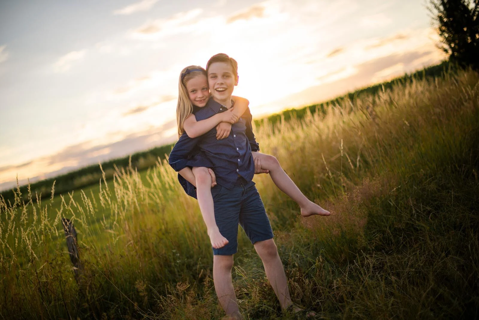 Kinderfotoshooting im Gegenlicht: Bruder trägt die lachende Schwester huckepack