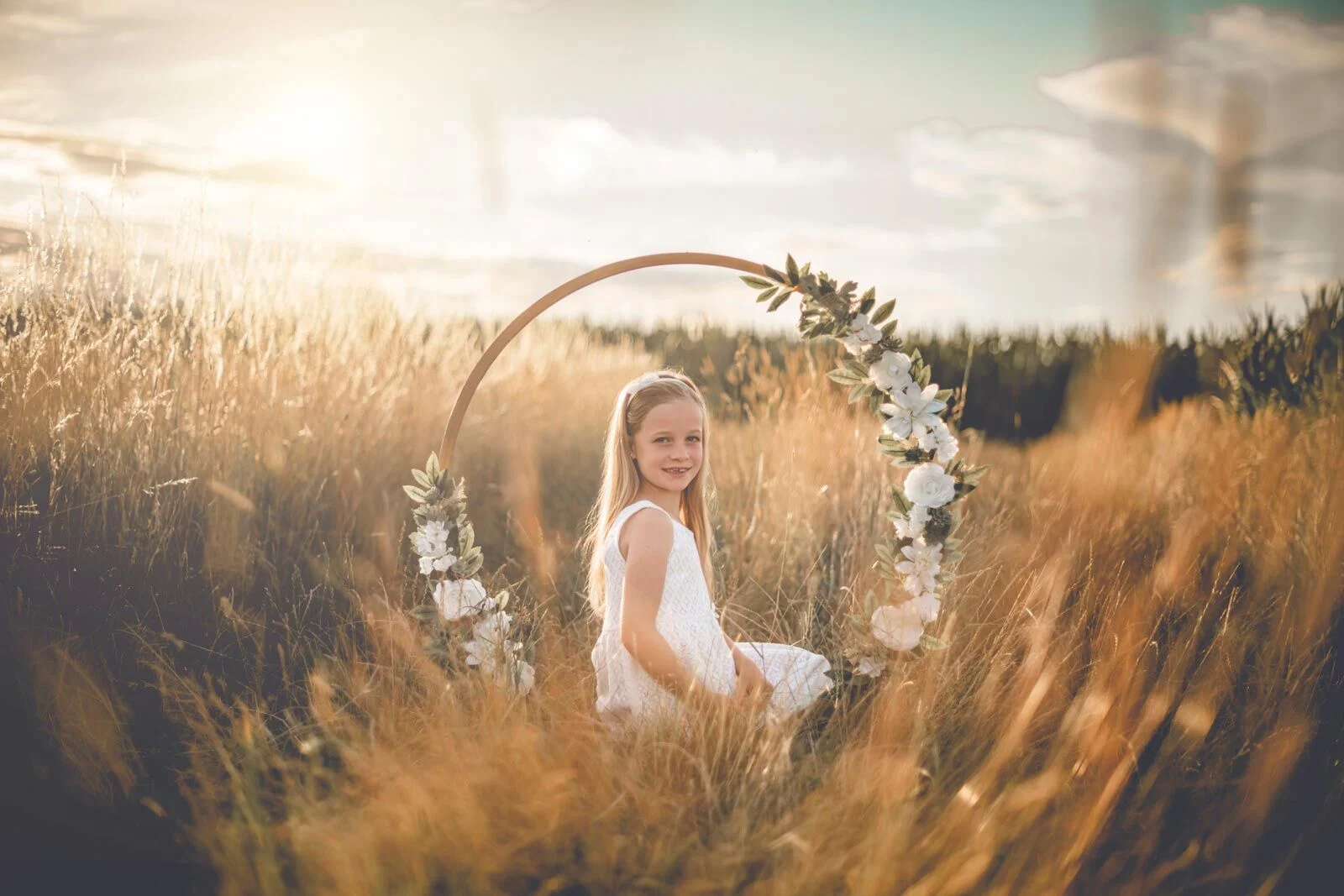 Kinderfotoshooting: Mädchen sitzt im Blumenring zwischen hohen, goldenen Gräsern