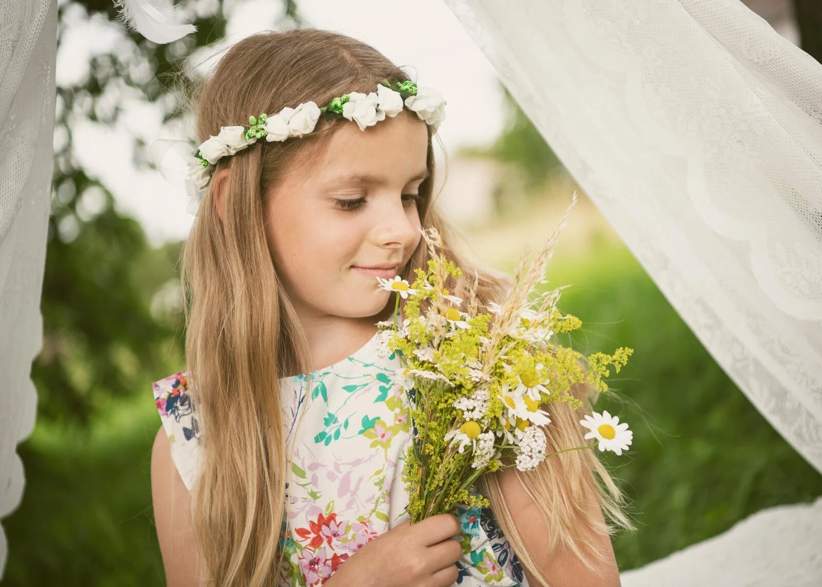 Mädchen im geblümten Kleid schaut verträumt auf einen Strauß Margeriten