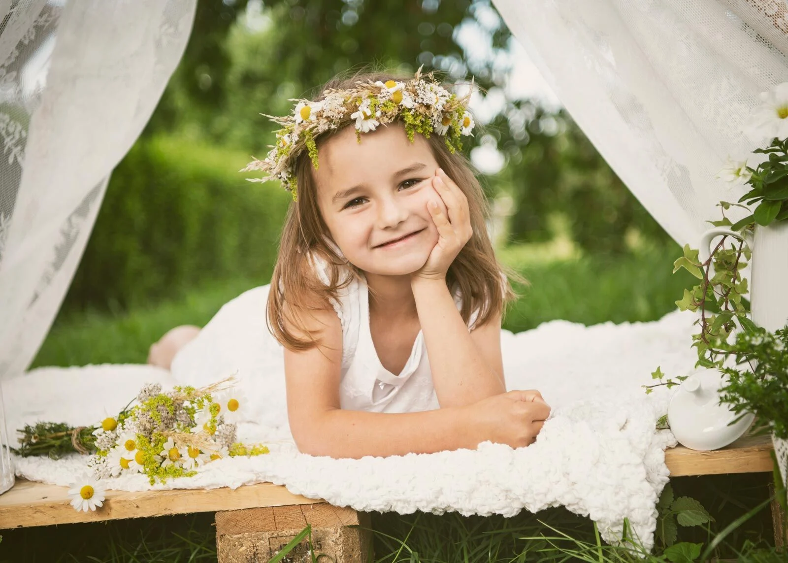 Mädchen mit Blumenkranz liegt auf einem Fell und stützt den Kopf in die Hand