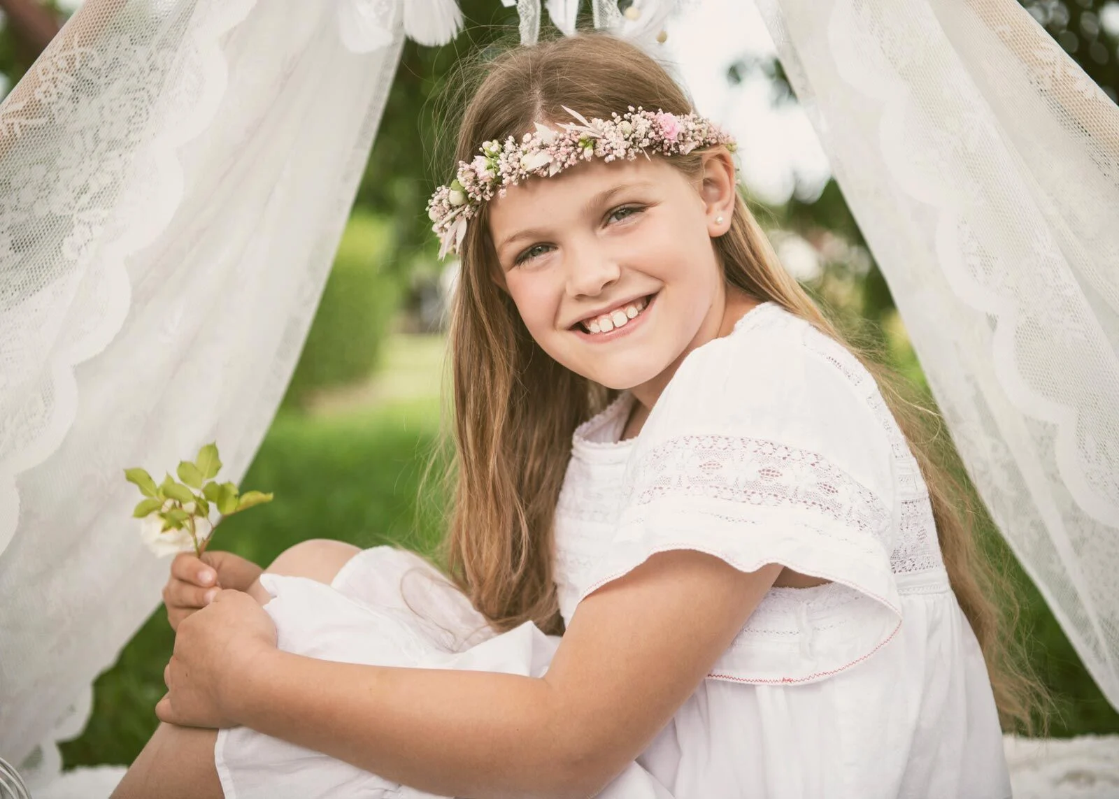 Lachendes Mädchen mit Blumenkranz und weißem Kleid hält einen Zweig