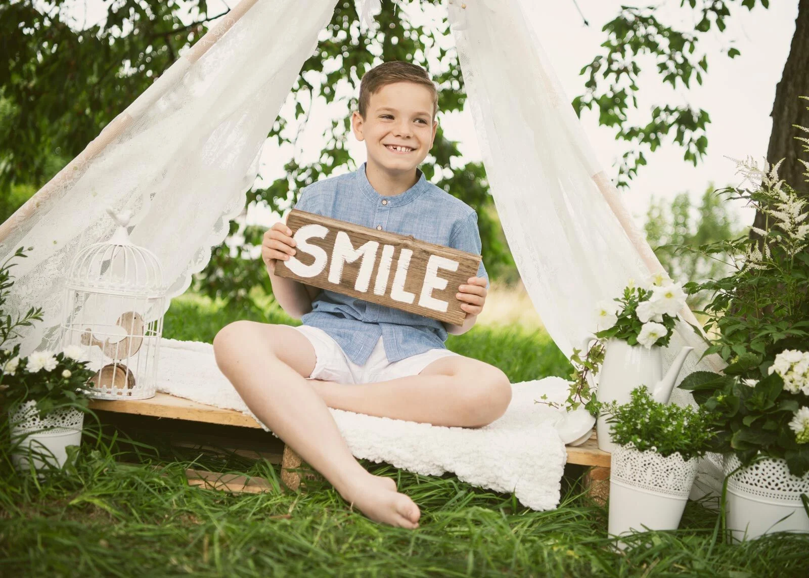 Junge im hellblauen Hemd hält ein Holzschild mit der Aufschrift Smile