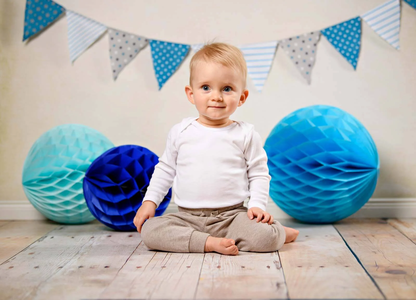 Fotoshooting zum 1. Geburtstag: Junge sitzt zwischen blauen Wabenbällen unter einer Wimpelkette