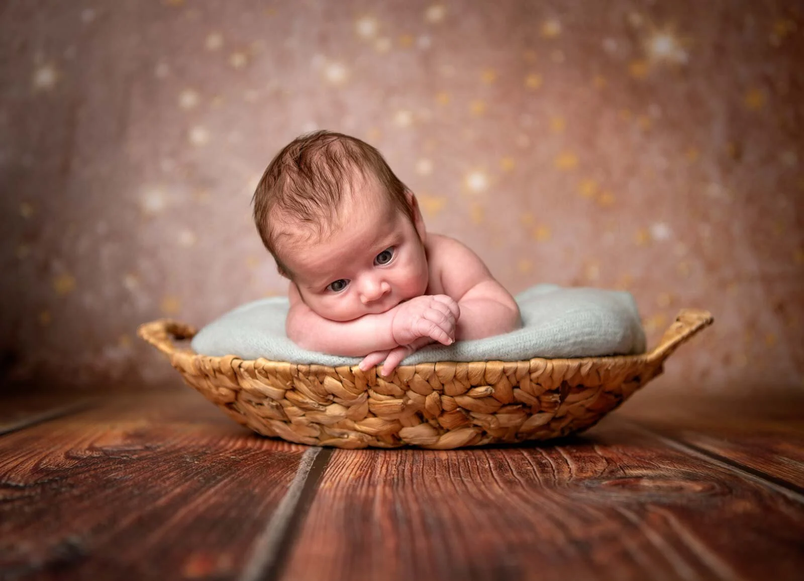 Baby hat den Kopf auf die Ärmchen gelegt und liegt in einem flachen Korb