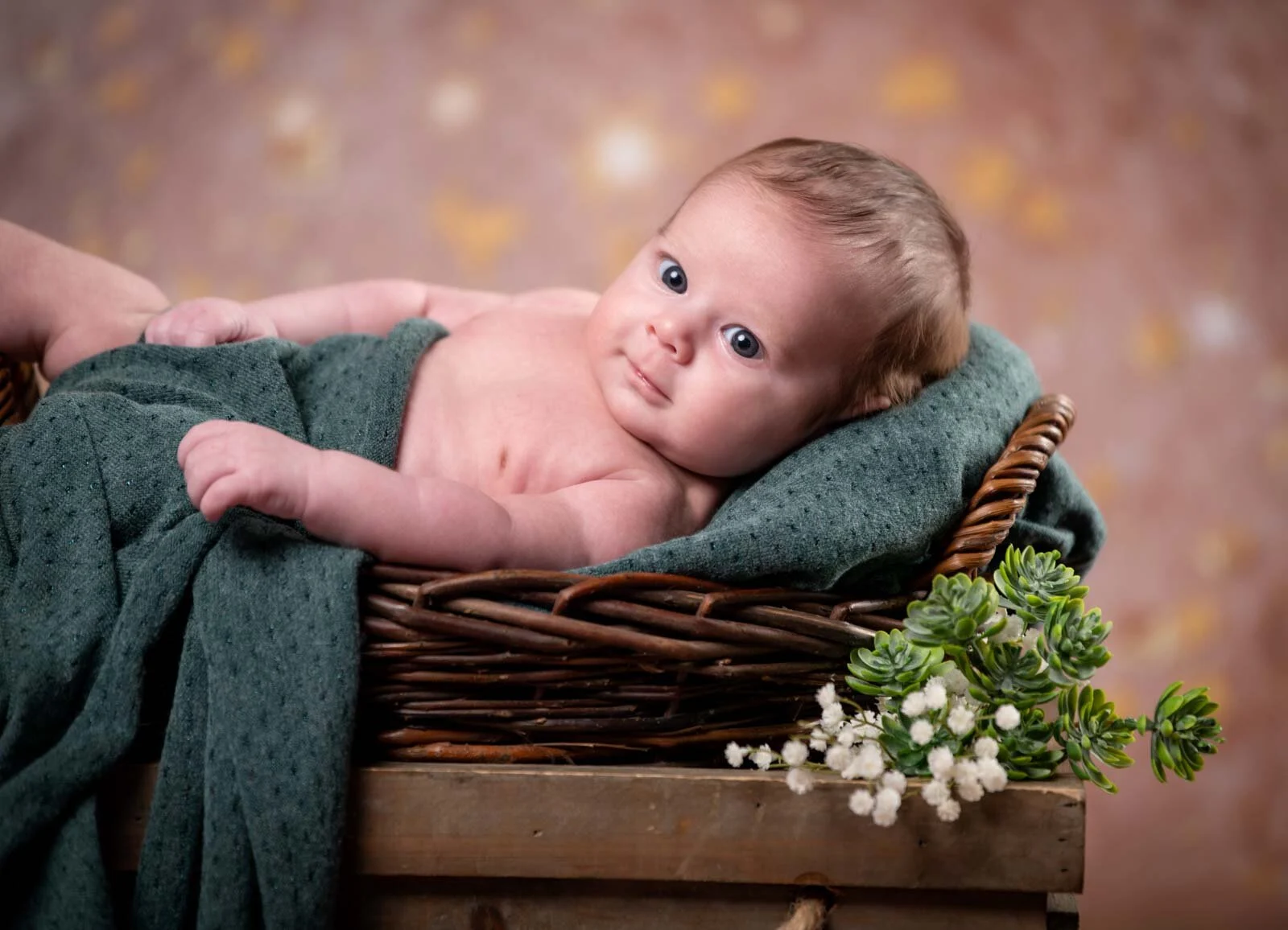 Babyshooting im Studio: Baby liegt seitlich im Weidenkorb und schaut in die Kamera