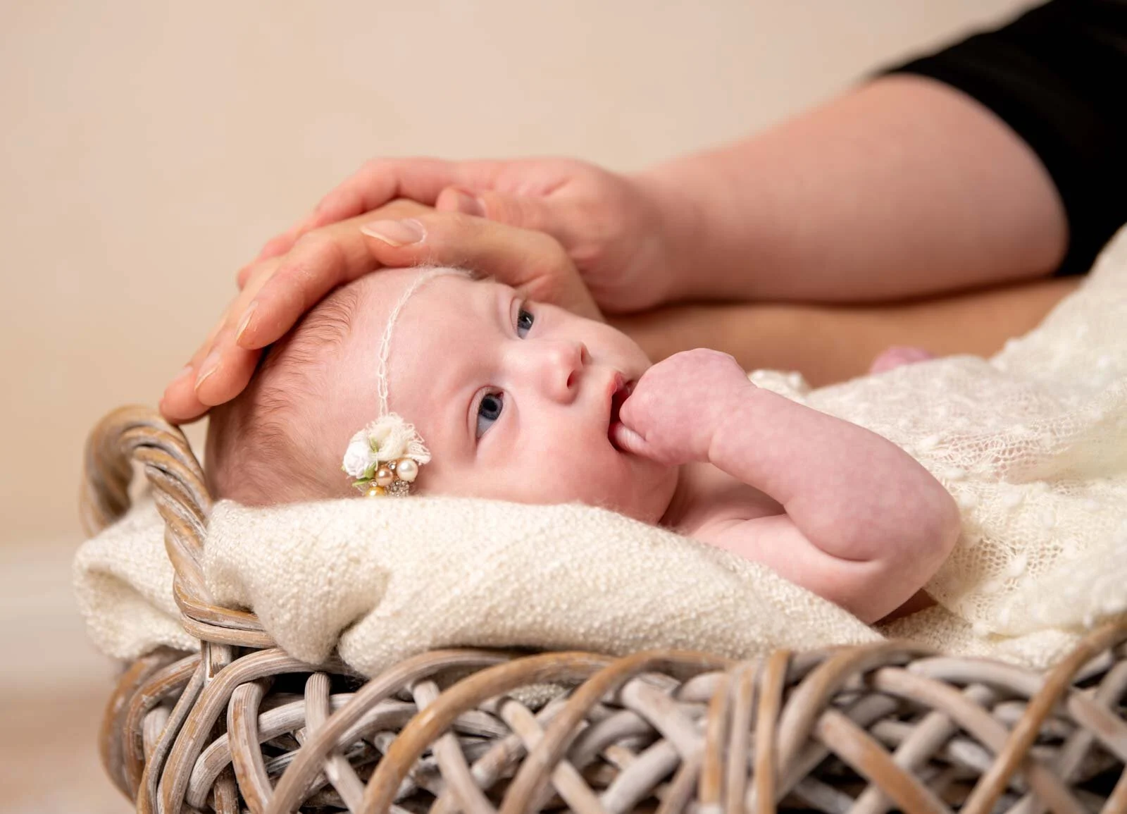 Mamas Hand | Peter Lauritis Photography Eine Hand streichelt sanft den Kopf eines Babys im Weidenkorb